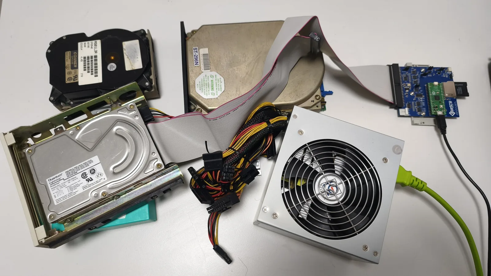 Drei alte SCSI-Festplatten von Conner, Seagate und Quantum, über ein Flachbandkabel mit einem BlueSCSI-Adapter verbunden, daneben ein PC-Netzteil zur Stromversorgung.